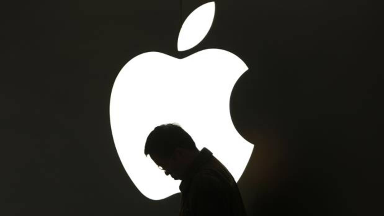 Un hombre mira su móvil delante del logotipo de Apple en Shangai
