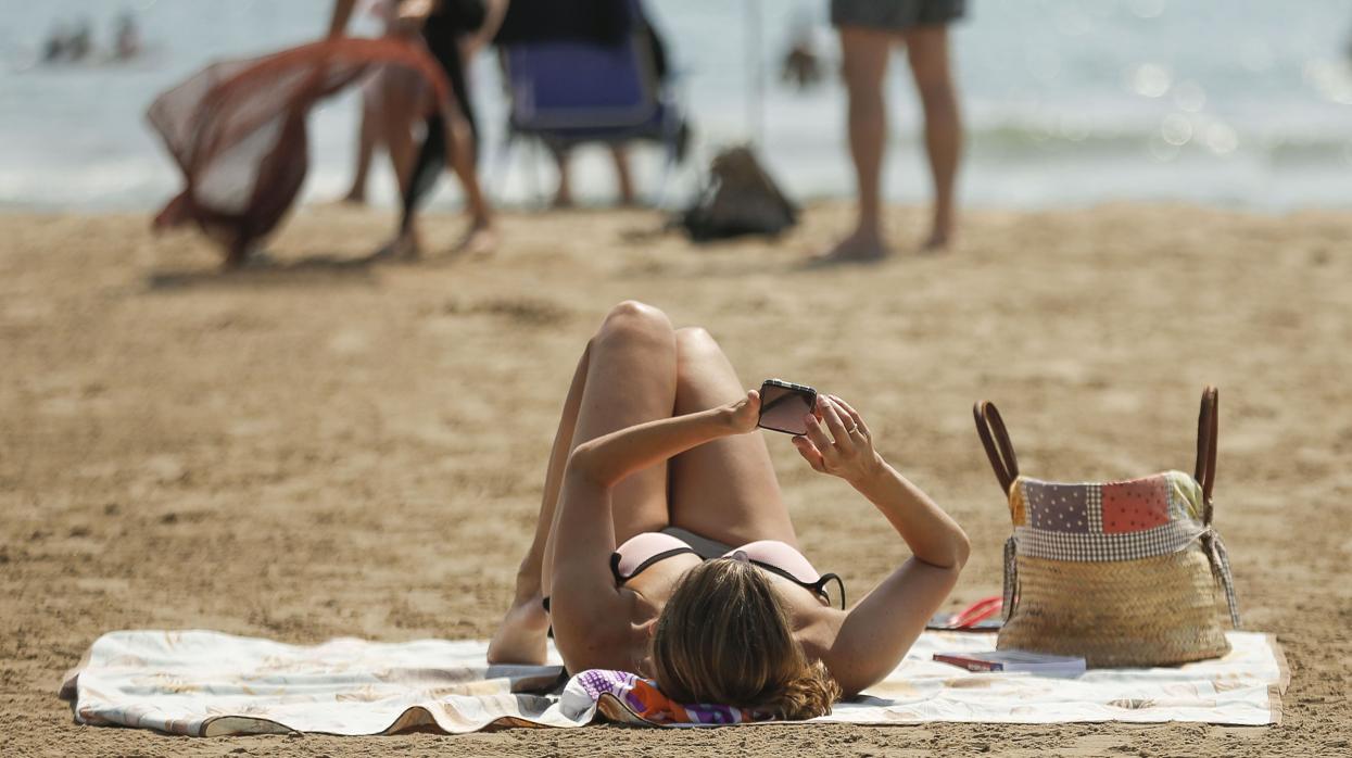 Una mujer revisa su móvil en la playa