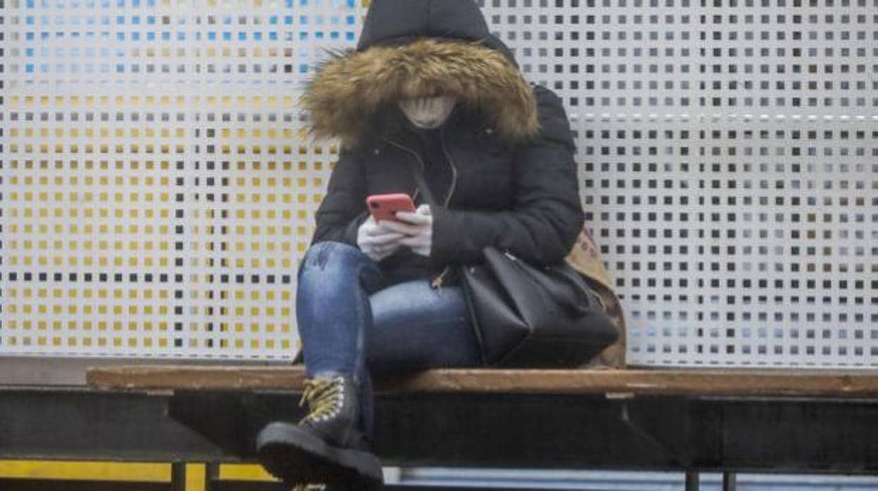 Imagen de una mujer consultando el móvil con guantes y mascarilla en Valencia