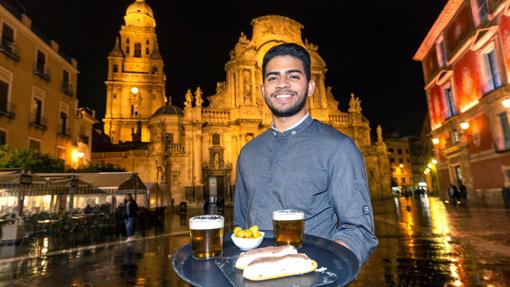 El camarero Luis Londoño del restaurante murciano Pasaje Belluga, posa con dos marineras, una tapa típica de Murcia, en la plaza Cardenal Belluga de Murcia. Al fondo la catedral