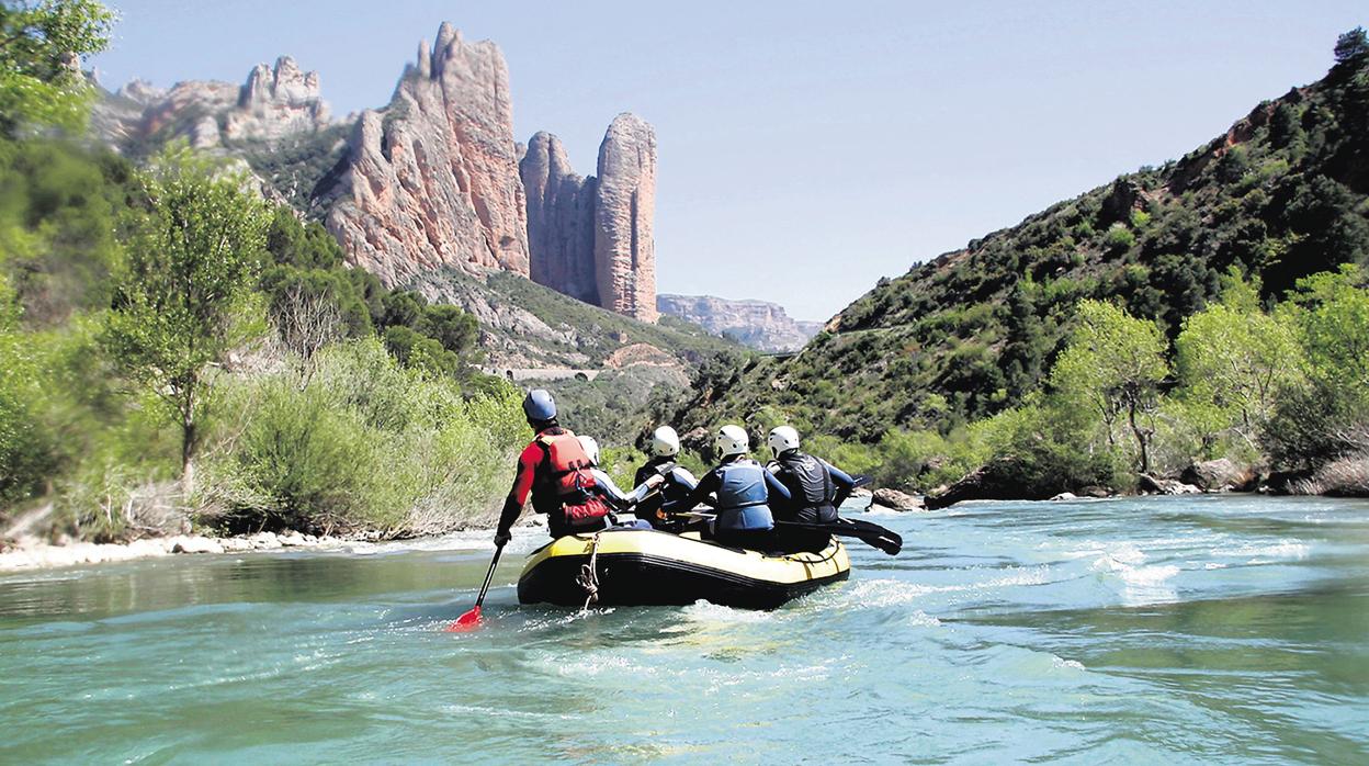 Una balsa se desliza por el cauce del río Gállego ante el paisaje de los Mallos de Riglos, en Huesca